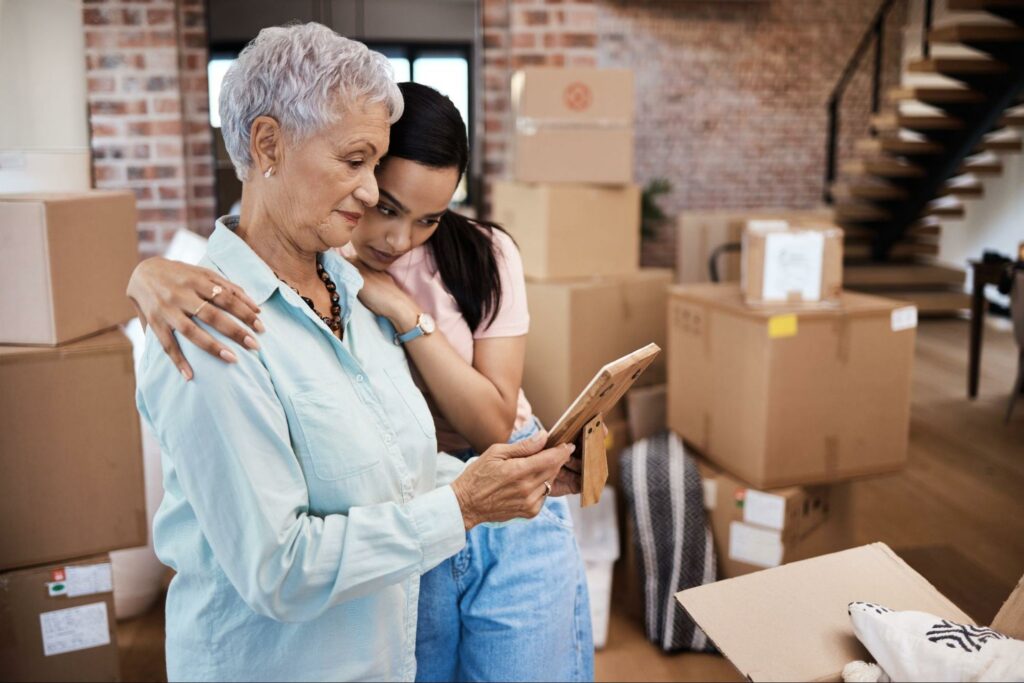 An older adult and her adult child are looking at a photo and reminiscing while packing to move into assisted living.