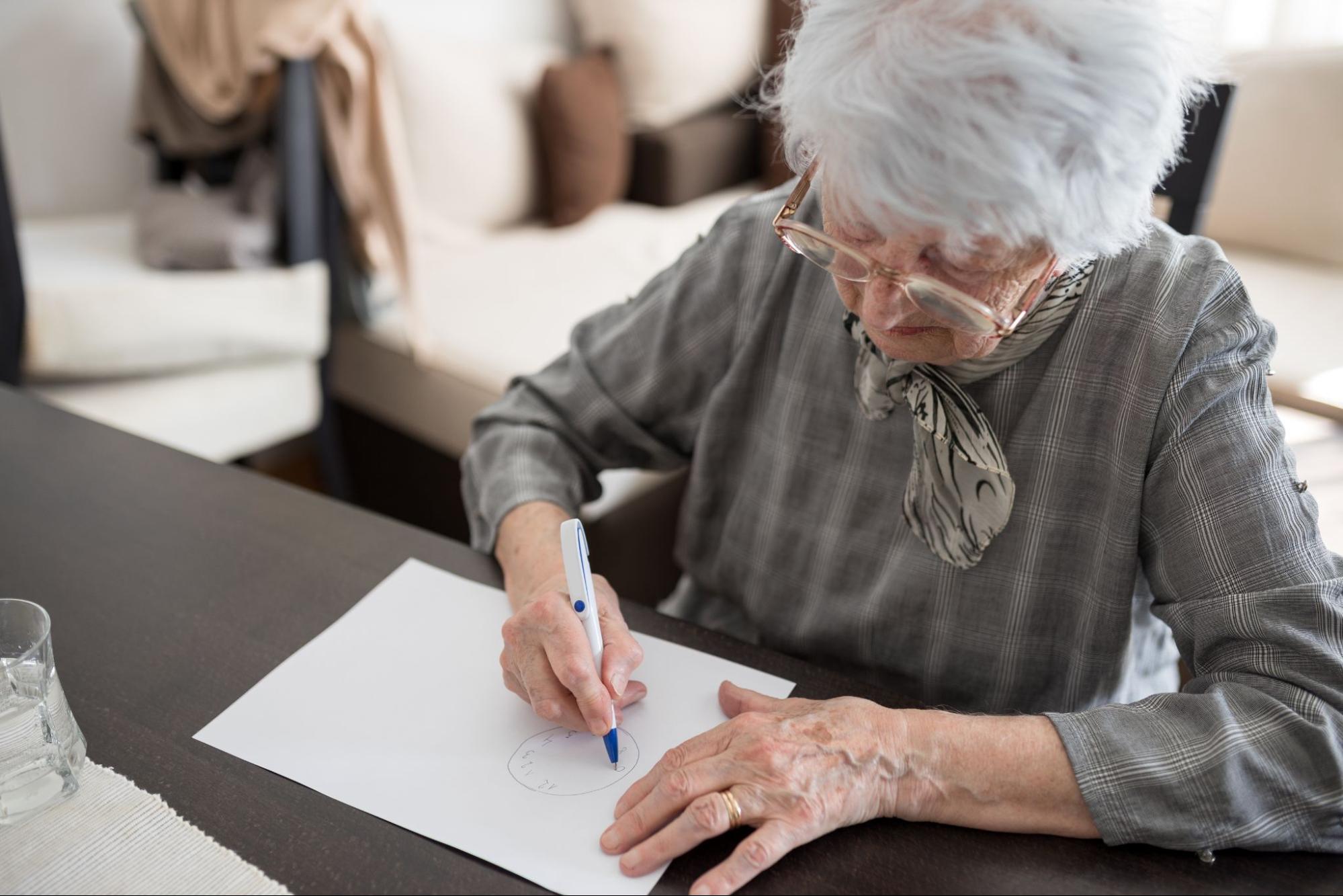 A senior at home writes on a piece of paper as part of a test for dementia.