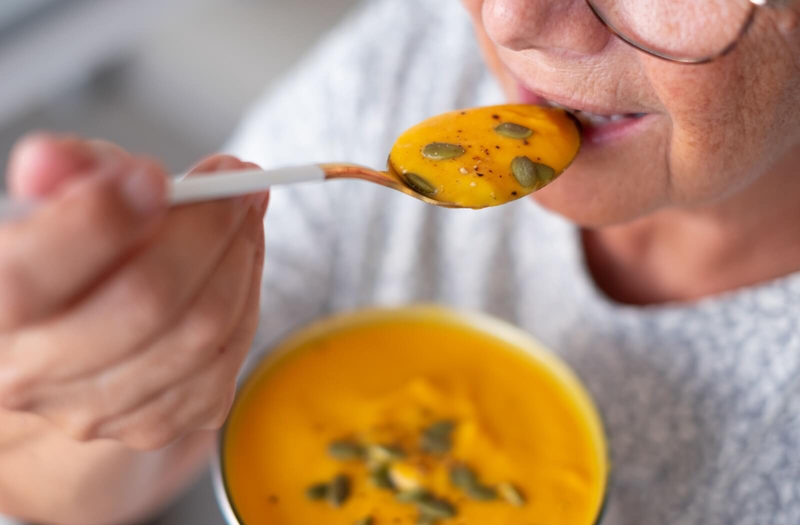 An older adult enjoying a bowl of thickened soup.