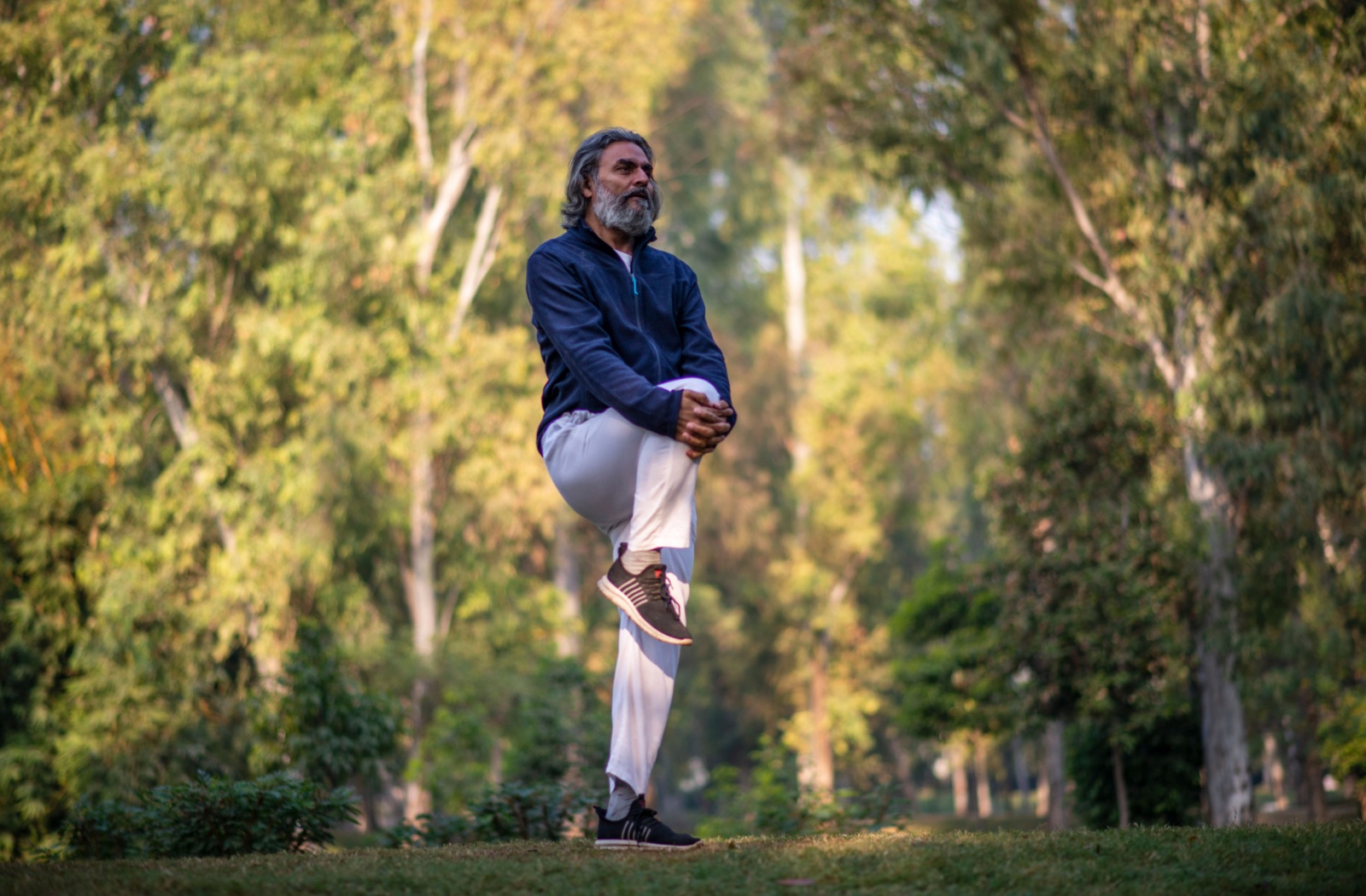 A senior man standing and balancing on one leg as he stretches his knee.
