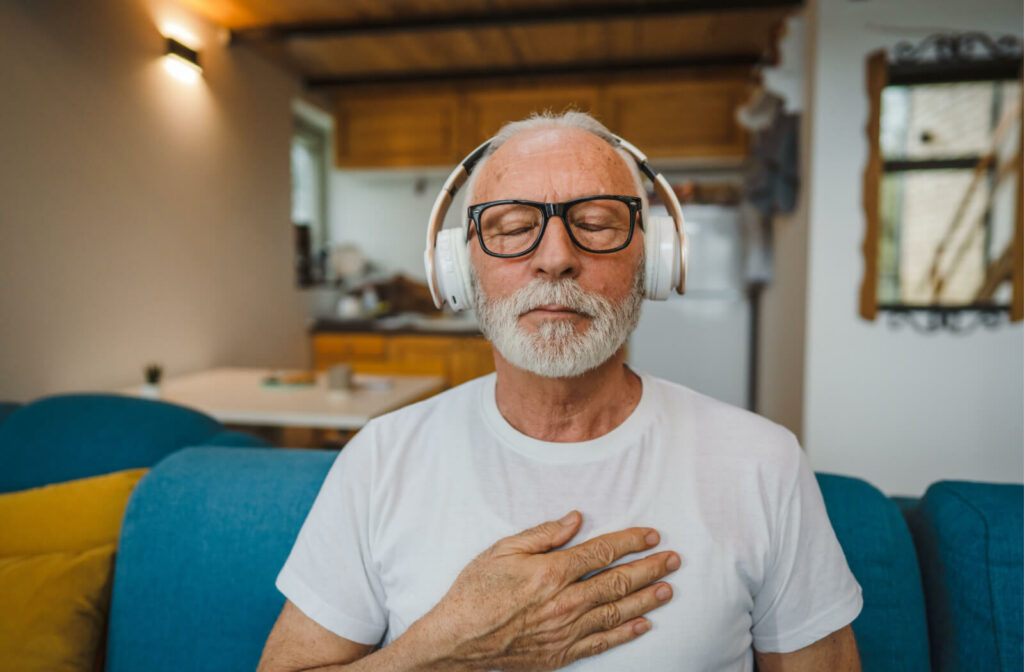 senior sits on a couch listening to music on headphones