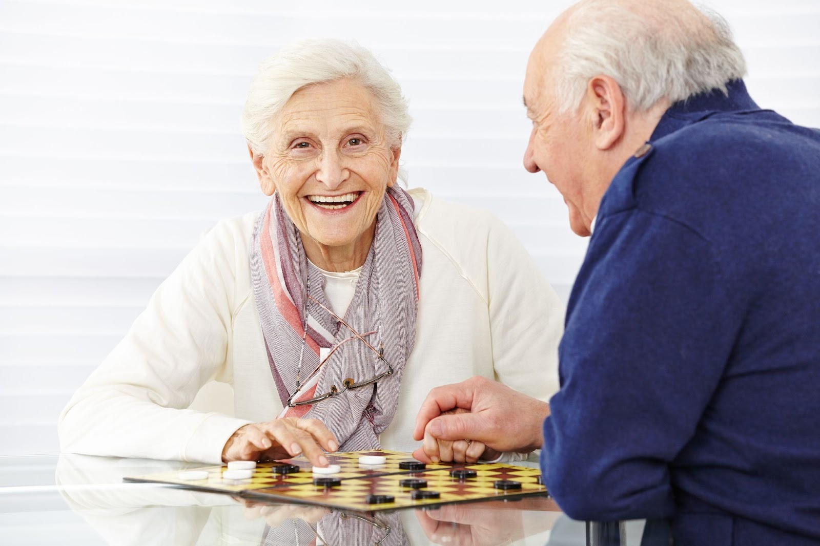 Two seniors smile as they play a game of checkers together.
